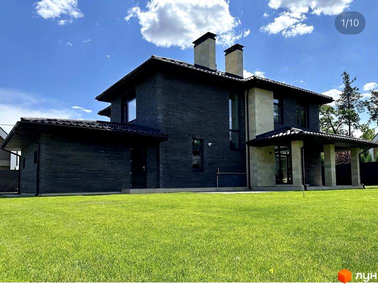 Котеджне містечко Spacious HOME: двоповерховий будинок з темної цегли та світлими вставками, з навісом та двома димарями, на тлі зеленого газону та блакитного неба.