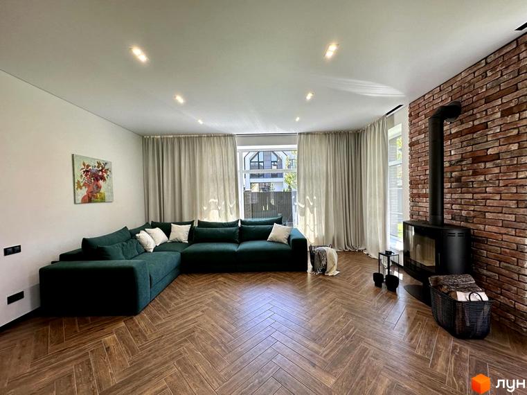 Простора вітальня з великим зеленим диваном та каміном у котеджному містечку Spacious HOME. Інтер'єр виконаний у сучасному стилі з акцентом на натуральні матеріали.