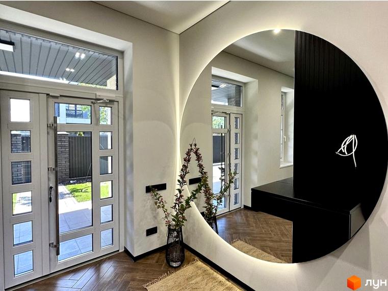 Просторий хол з великим круглим дзеркалом та подвійними дверима, що ведуть на зелену галявину.