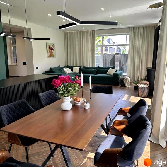 Простора вітальня з великим зеленим диваном, каміном та обіднім столом з квітами. КМ Spacious HOME – це сучасна новобудова з комфортним плануванням.