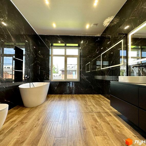 Простора ванна кімната в білих тонах з мармуровим оздобленням стін та дерев'яною підлогою. Велике вікно забезпечує природне освітлення.