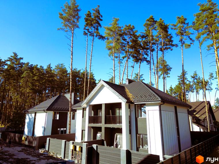 Сучасні дуплекси Toscana Home з біло-сірим фасадом та темним дахом на тлі соснового лісу. Прибудинкова територія огороджена парканом.