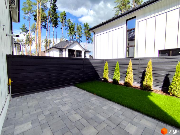 Зовнішній вигляд будинку в ЖК Toscana Home з темним парканом та доглянутою прибудинковою територією з газоном та бруківкою.