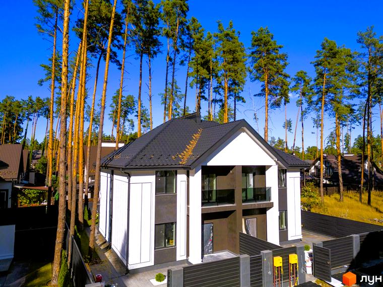 Сучасний дуплекс Toscana Home з біло-сірим фасадом та чорним дахом, оточений високими соснами та огородженою територією.