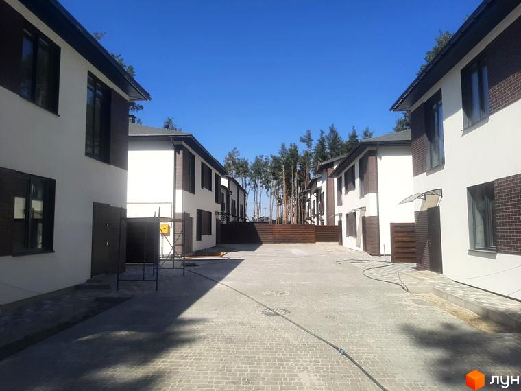 Котеджне містечко КМ Лісове-3. Сучасні двоповерхові будинки з білою та коричневою обробкою фасадів, розташовані на вимощеній бруківкою території з зеленими насадженнями.