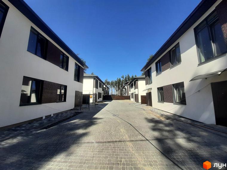 Котеджне містечко Лісове-3: двоповерхові будинки з білою штукатуркою та коричневими вставками з цегли. Навколо будівель викладена бруківка, що веде до будинків.