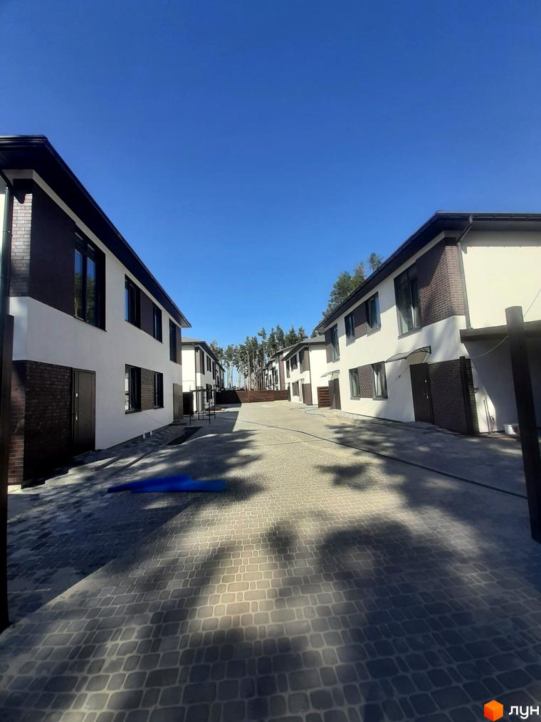 Котеджне містечко КМ Лісове-3. Зовнішній вигляд будинків з білою штукатуркою та коричневими вставками, вимощена бруківкою прибудинкова територія.