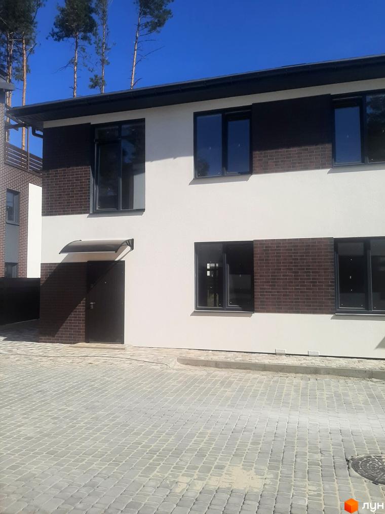 Котеджне містечко КМ Лісове-3: двоповерховий будинок з білою штукатуркою, темними вікнами та цегляними вставками. Прибудинкова територія вимощена бруківкою.