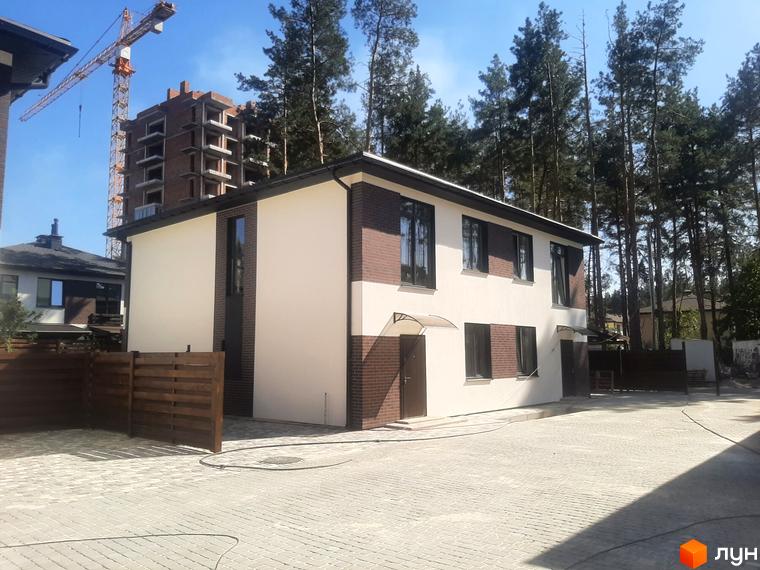 Котеджне містечко КМ Лісове-3: двоповерховий будинок з білою та коричневою цегляною обробкою та прибудинковою територією з бруківки та дерев'яного паркану.