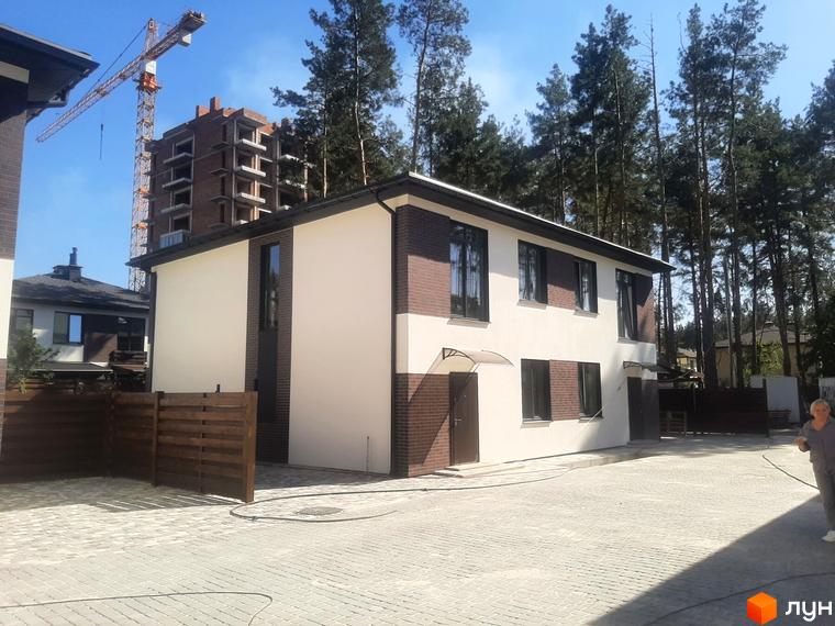 Котеджне містечко КМ Лісове-3. Зовнішній вигляд двоповерхових будинків з білою та цегляною обробкою, вікнами та дверима. Прибудинкова територія з бруківкою та дерев'яним парканом.