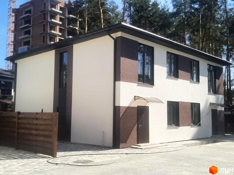 Котеджне містечко Лісове-3: двоповерховий будинок з білим фасадом та цегляними вставками, вікна з темними рамами. Навколо будинку бруківка та дерев'яний паркан.