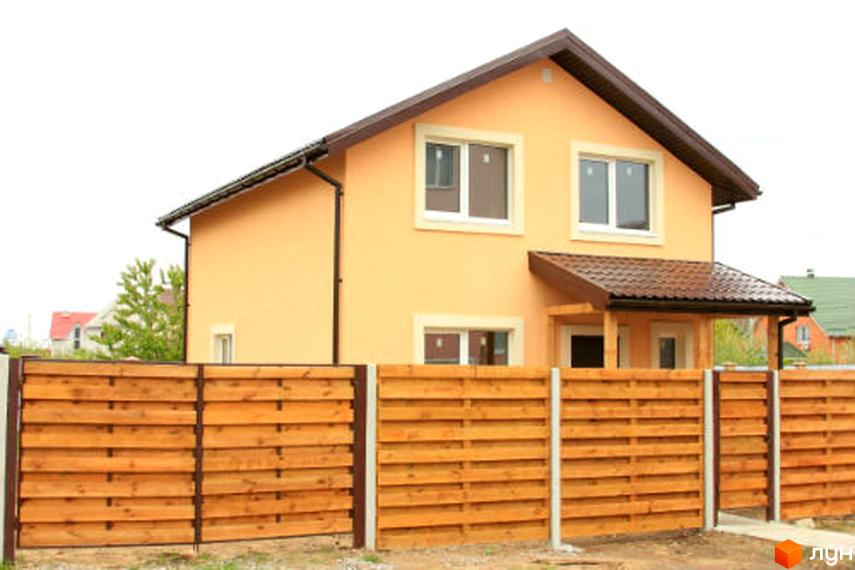 Двоповерховий будинок персикового кольору з коричневим дахом та білими вікнами в Котеджному містечку Софіївка. Перед будинком встановлено дерев'яний паркан.