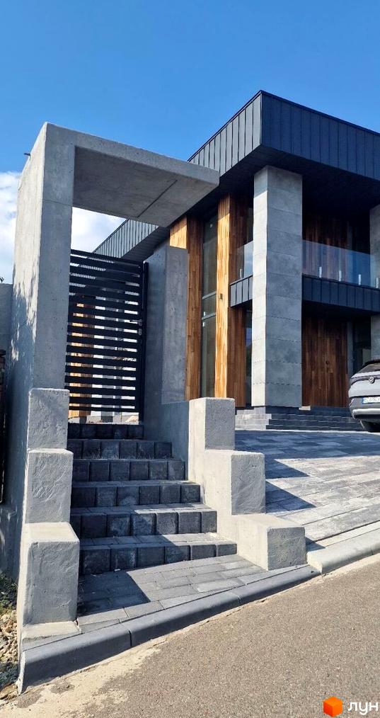 Зображення будинку з великими вікнами та сірим фасадом у котеджному комплексі Zubra House. Перед будинком сходи та бруківка.