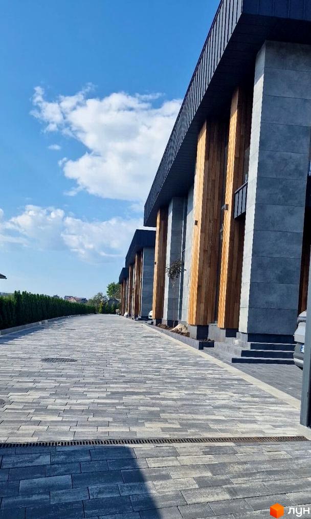 Зображення дуплексів Zubra House з фасадом з дерева та сірого каменю. На передньому плані вимощена плиткою прибудинкова територія.