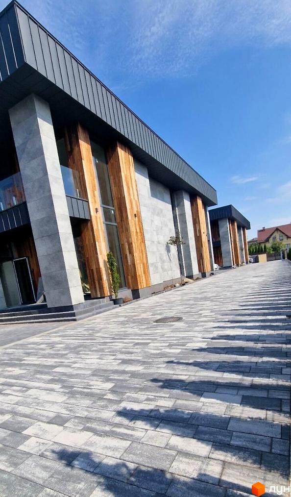 Зображення дуплексу Zubra House з сірими стінами та дерев'яними вставками. На передньому плані викладена бруківкою прибудинкова територія.