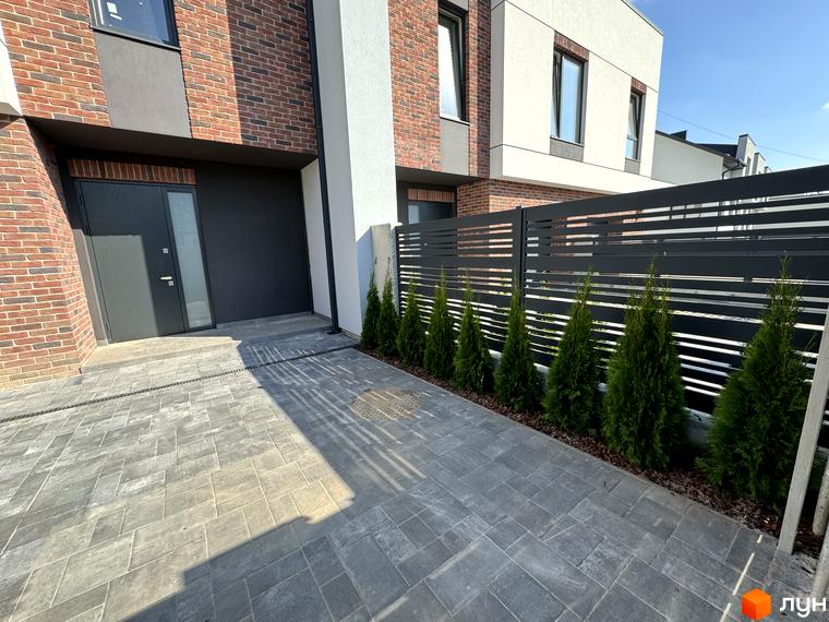 Зовнішній вигляд таунхаусів Loft House з цегляним фасадом та великими вікнами. Прибудинкова територія з бруківкою та туями.