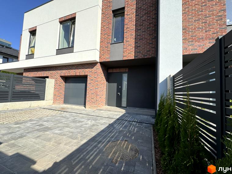 Таунхауси Loft House з цегляним фасадом, гаражем та брукованою прибудинковою територією. Сучасна новобудова з чорним парканом та зеленими насадженнями.