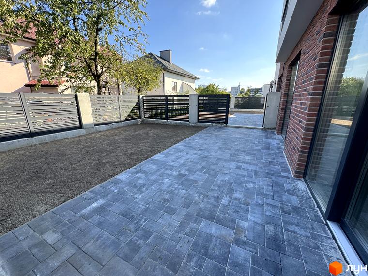 Таунхауси Loft House: сучасний фасад з цегли та великі вікна, поруч вимощена сіра плитка та зелена ділянка з парканом.