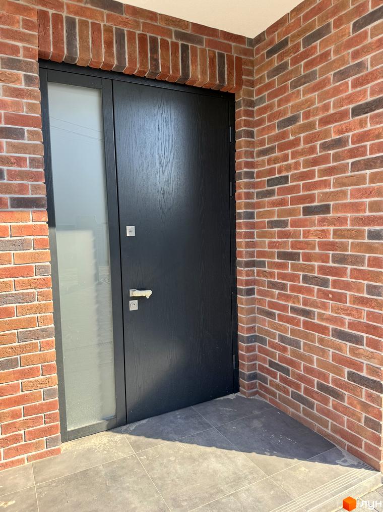 Таунхауси Loft House: вхідна група з темними дверима та бічним склом на тлі цегляної стіни. Прибудинкова територія викладена плиткою.