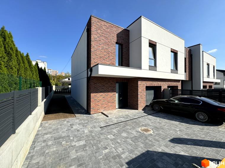 Таунхауси Loft House з цегляним фасадом та білими панелями, прибудинкова територія з бруківки та паркуванням для автомобілів.