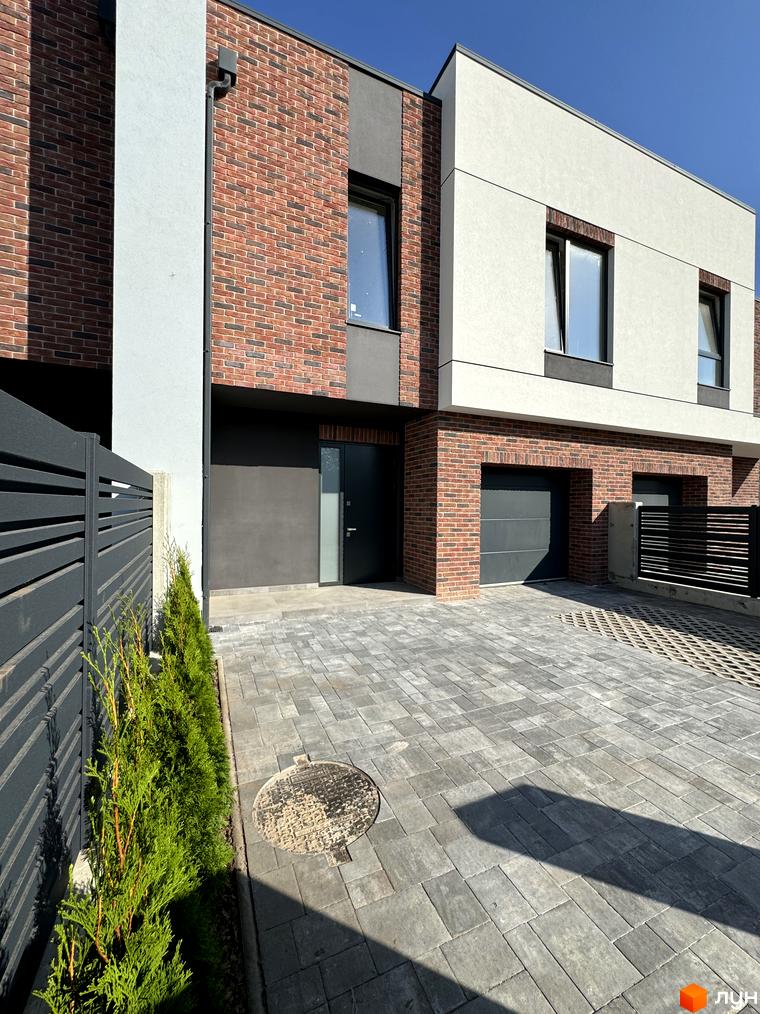 Таунхауси Loft House з цегляним фасадом та білою штукатуркою, з гаражними воротами та бруківкою перед будинком.