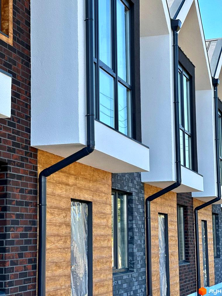 Фасад Таунхаусів „Ірпінський Модерн“ з комбінацією темно-червоної цегли, світлої штукатурки та дерев'яних панелей, з чорними вікнами та водостоками.