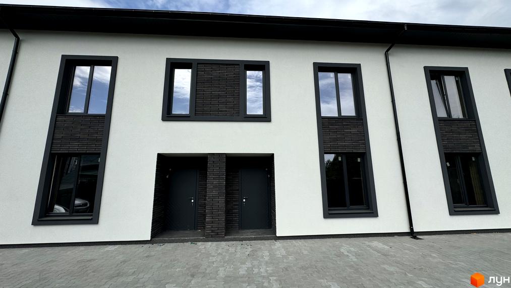 Таунхауси А56: фасади будинків з темними вікнами та цегляними вставками, вимощені сірою плиткою подвір'я.