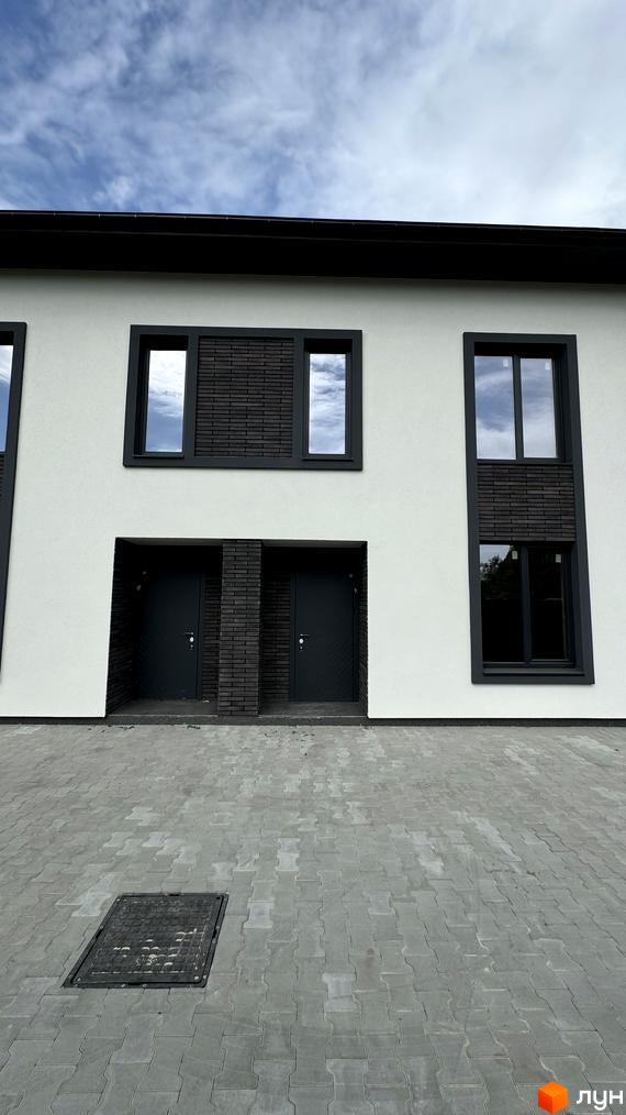 Таунхауси А56: фасади з темними віконними рамами та дверима, сіра бруківка перед будинками. Зовнішній вигляд новобудови та прибудинкової території.