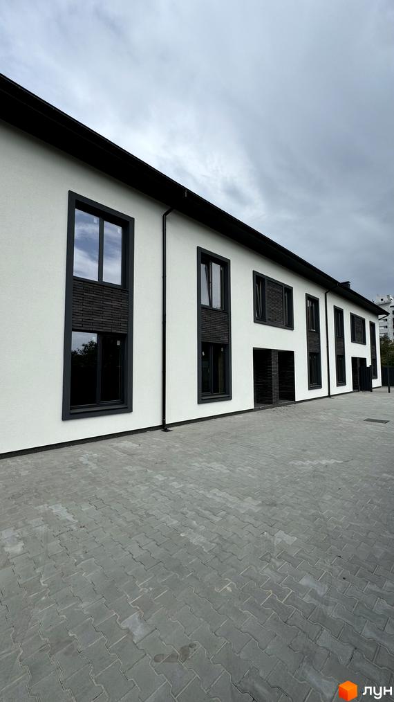 Таунхауси А56: фасади будівель з темними віконними рамами та сірою бруківкою на прибудинковій території.