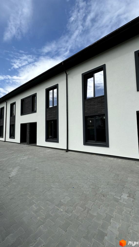 Таунхауси А56 з білою фасадною штукатуркою та темними віконними рамами, розташовані на вимощеній сірою плиткою прибудинковій території.