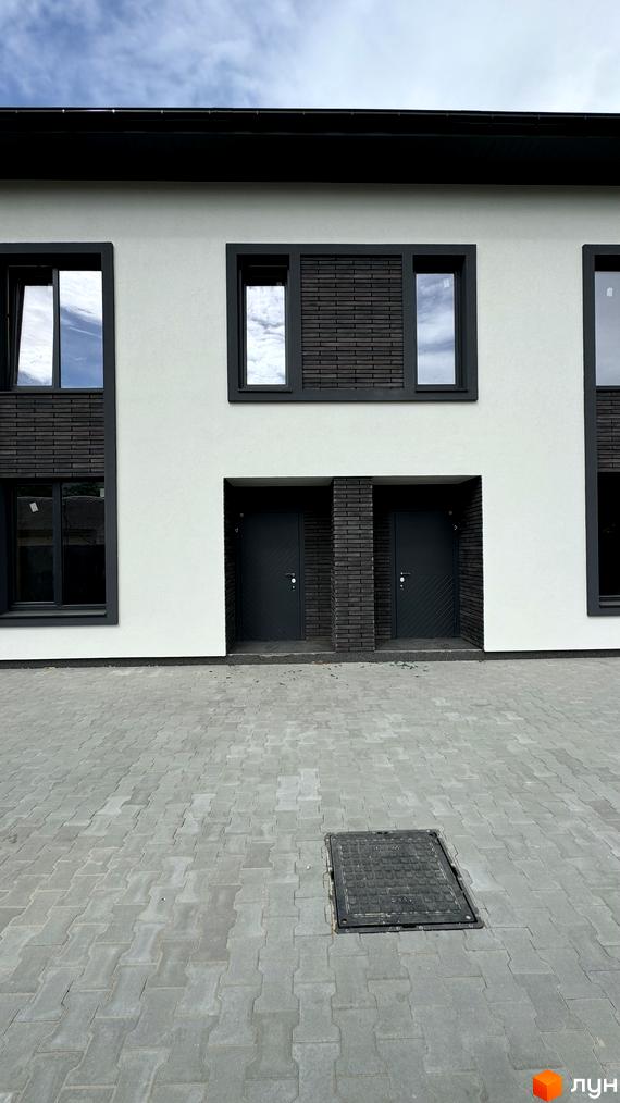 Фасад житлового комплексу Townhouses A56 з білими стінами та темними вікнами. Перед будинком розташована брукована територія.