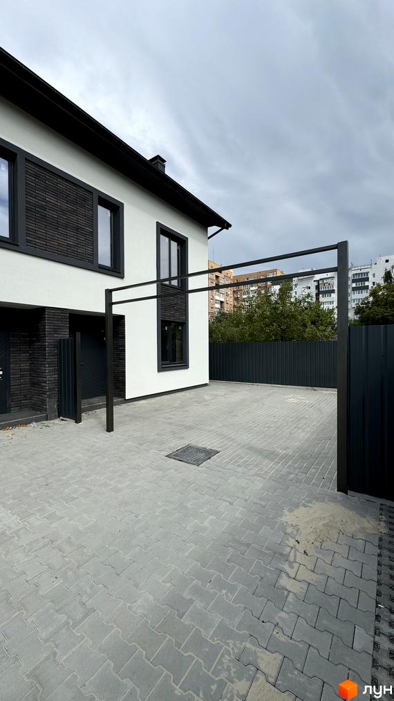 Таунхауси А56: білий будинок з чорними елементами та навісом на подвір'ї з бруківки.