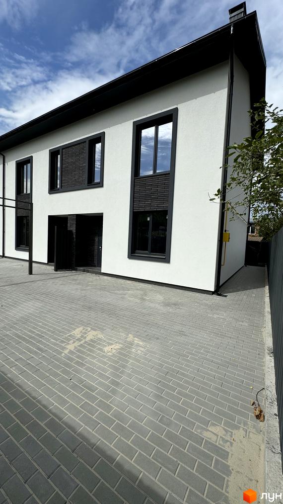 Таунхауси А56 – білий двоповерховий будинок з чорними вікнами та дахом, розташований на вимощеній сірою плиткою території.