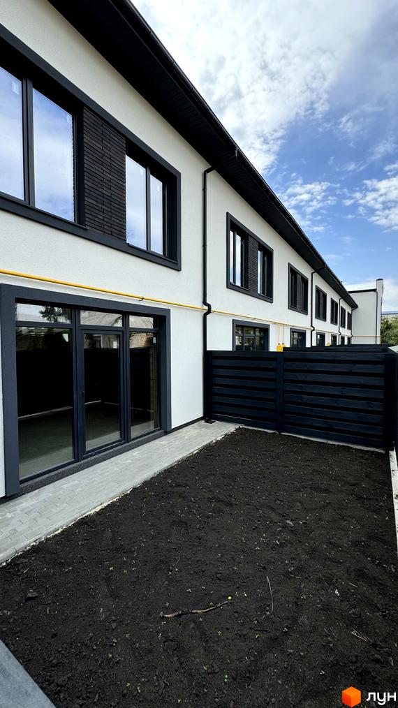 Таунхауси А56: фасади з великими вікнами та чорними елементами, прибудинкова територія з доглянутим газоном та парканом.