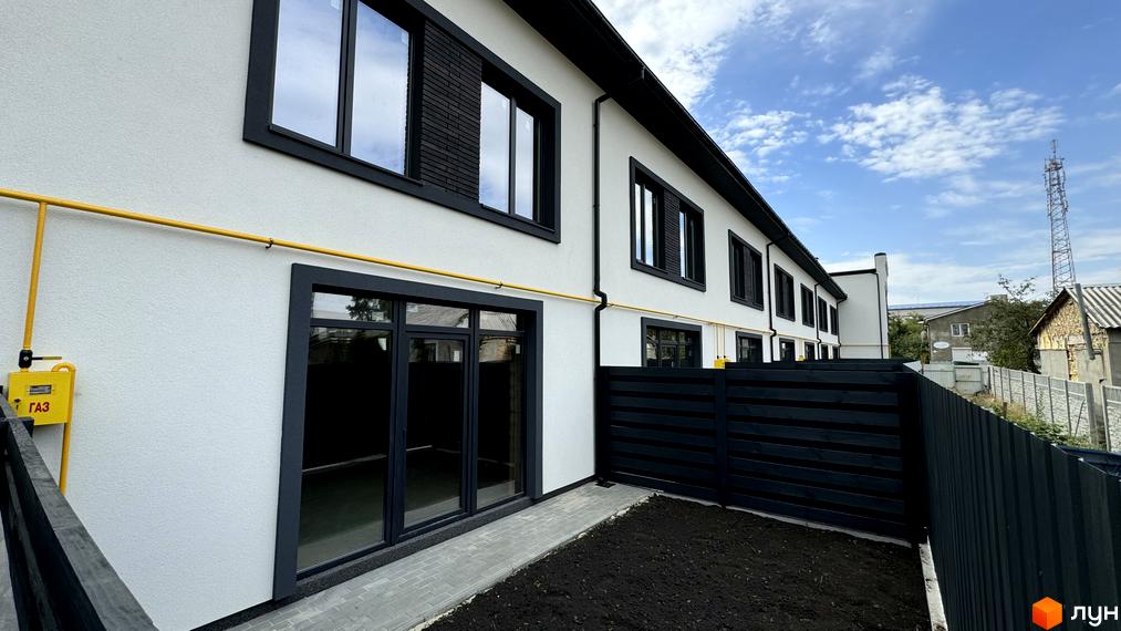 Таунхауси А56: фасади білих будівель з чорними вікнами та парканом, поруч зелена ділянка та газова труба.