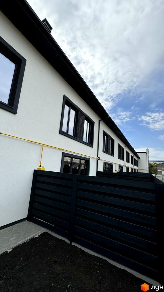 Таунхауси А56: білосніжні фасади з чорними вікнами та дахом, огороджені темним парканом. Поруч доглянута прибудинкова територія з газоном.