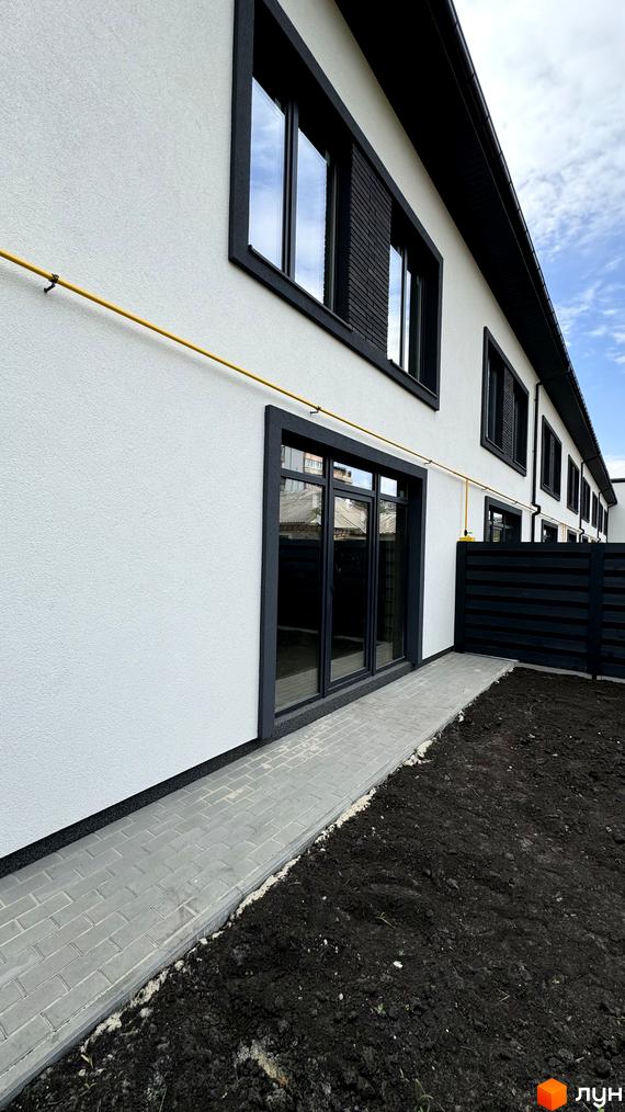 Зовнішній вигляд таунхаусів А56 з білою штукатуркою та темними вікнами, поруч вимощена доріжка та ділянка з чорноземом.