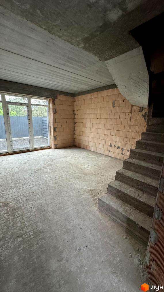 Будівельний проєкт Таунхауси А56: недобудований будинок з цегляними стінами та бетонною підлогою, вікно з видом на паркан.