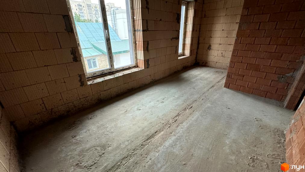 Будівельний проєкт Таунхауси А56: цегляні стіни та бетонна підлога в приміщенні з вікнами, що виходять на зелений дах сусідньої будівлі.