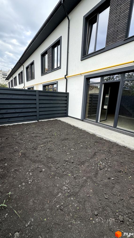 Таунхауси А56: білий фасад з чорними вікнами та дверима, огороджена територія з зеленою ділянкою. Зовнішній вигляд будинку та прибудинкової території.