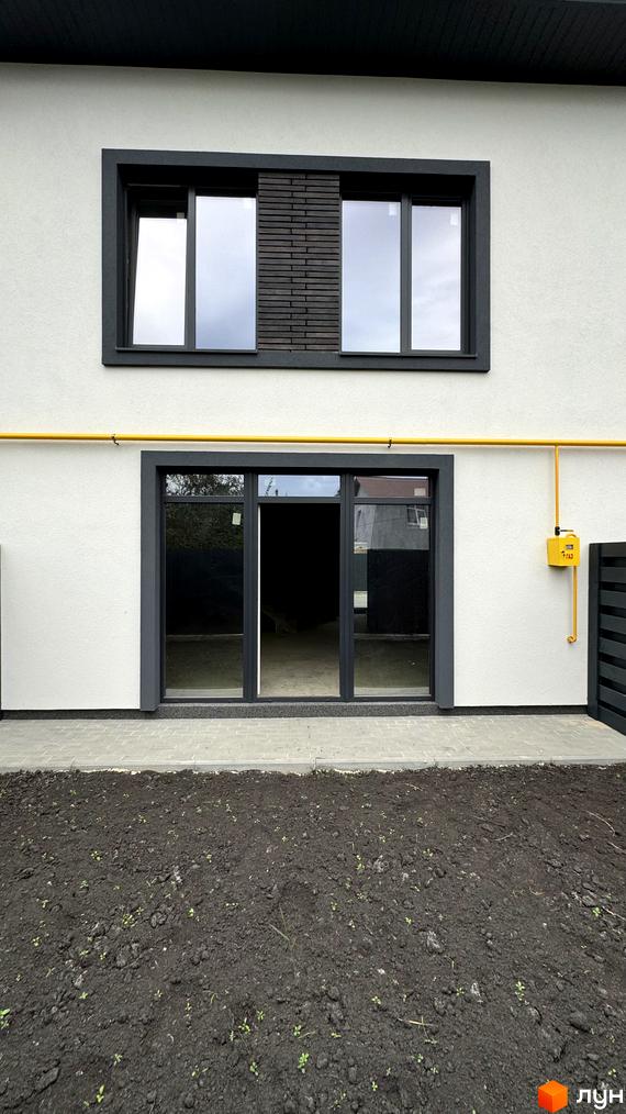 Таунхауси А56: фасад будинку з великими вікнами та дверима, жовта газова труба та ділянка з ґрунтом. Зовнішній вигляд новобудови.