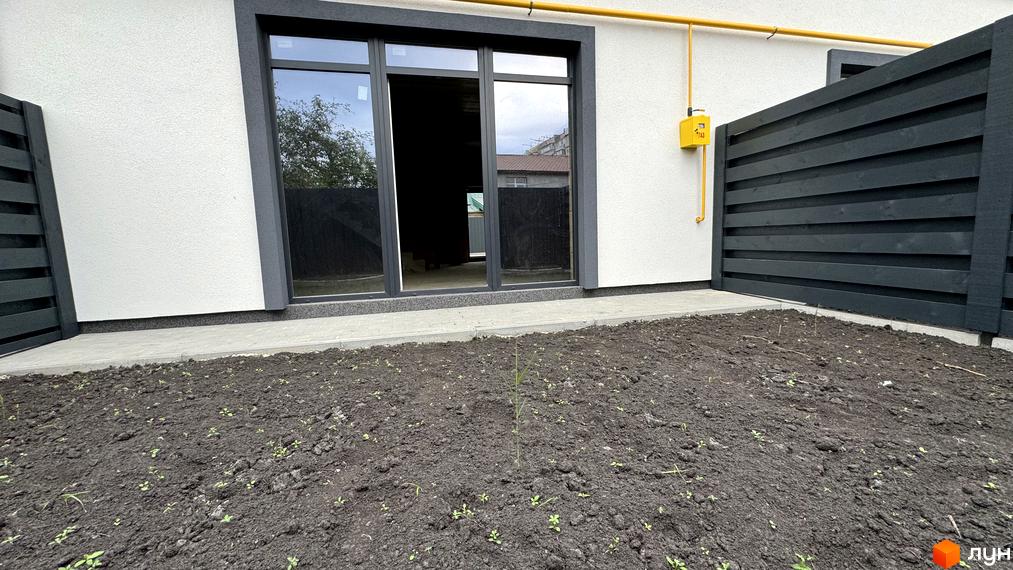 Зовнішній вигляд таунхаусів А56 з чорним парканом та зеленими насадженнями. Сучасний житловий комплекс з великими вікнами та газовою трубою.