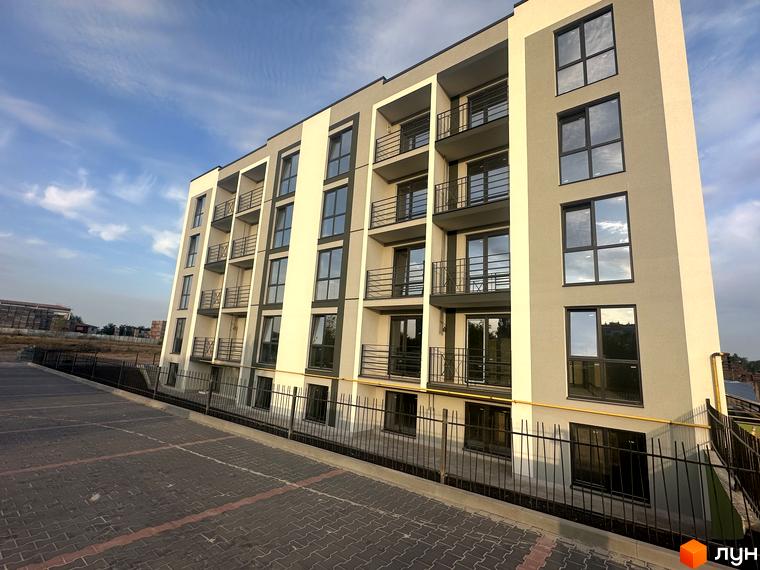 Фасад житлового комплексу Brickwood 2 з балконами та великими вікнами, поряд облаштований паркінг з бруківкою.