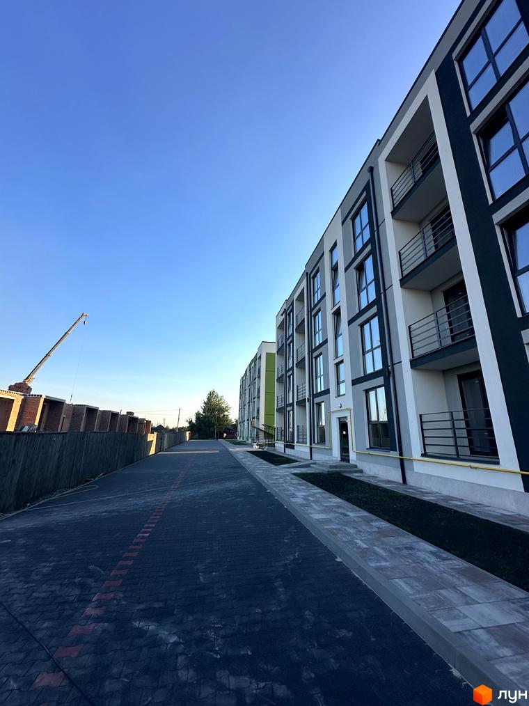 Новобудова ЖК Brickwood 2 з сірими та білими фасадами, балконами та великими вікнами. Поруч асфальтована дорога та будівельний майданчик з краном.