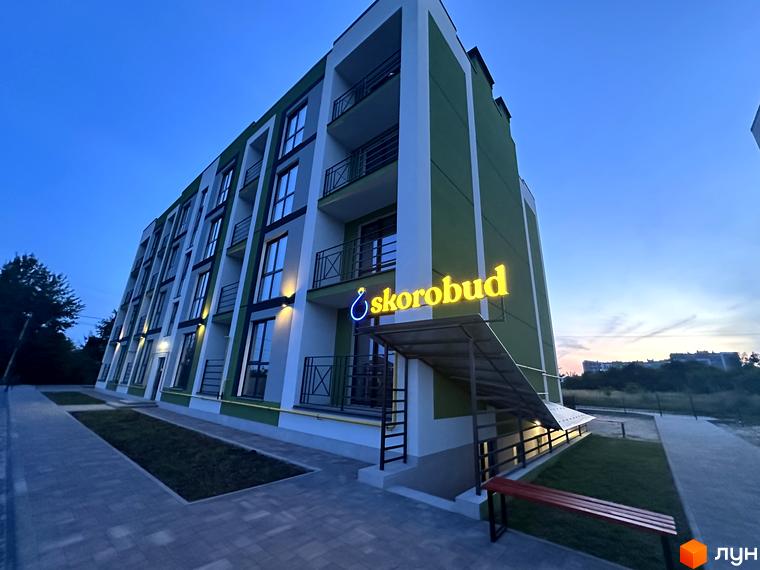 Житловий комплекс Brickwood 2 з зелено-білим фасадом та балконами, освітлений вечірнім світлом. Поруч розташована доглянута прибудинкова територія з доріжками та лавкою.