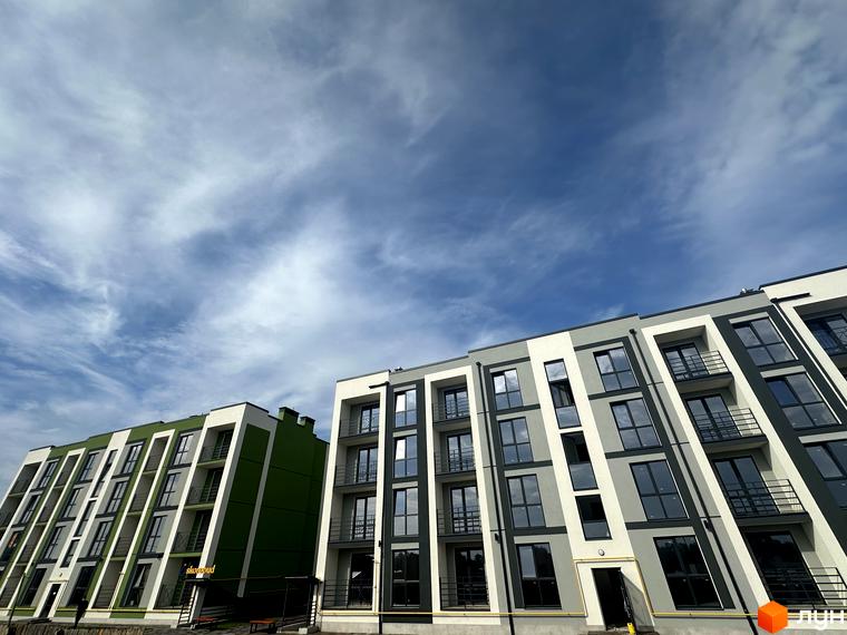 Зовнішній вигляд новобудови ЖК Brickwood 2 з фасадами сірого та зеленого кольорів під блакитним небом з хмарами.