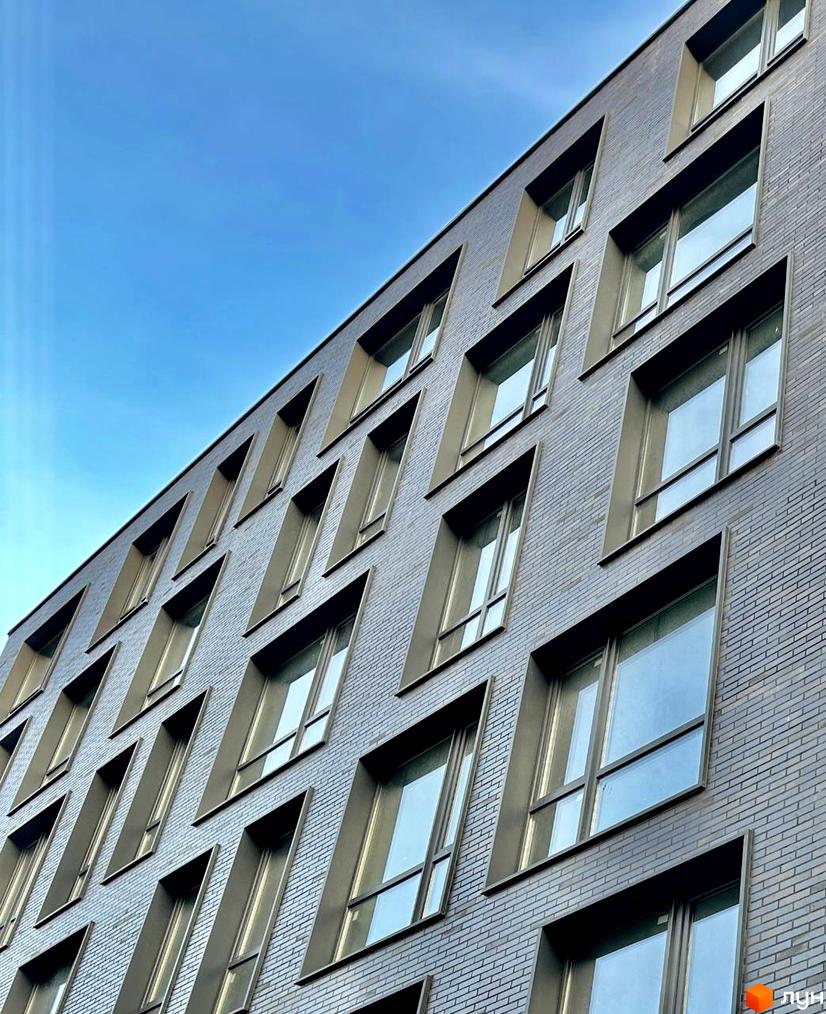 Фасад Житлового комплексу ArtHof з темно-сірої цегли та вікнами з похилими відкосами на тлі блакитного неба.