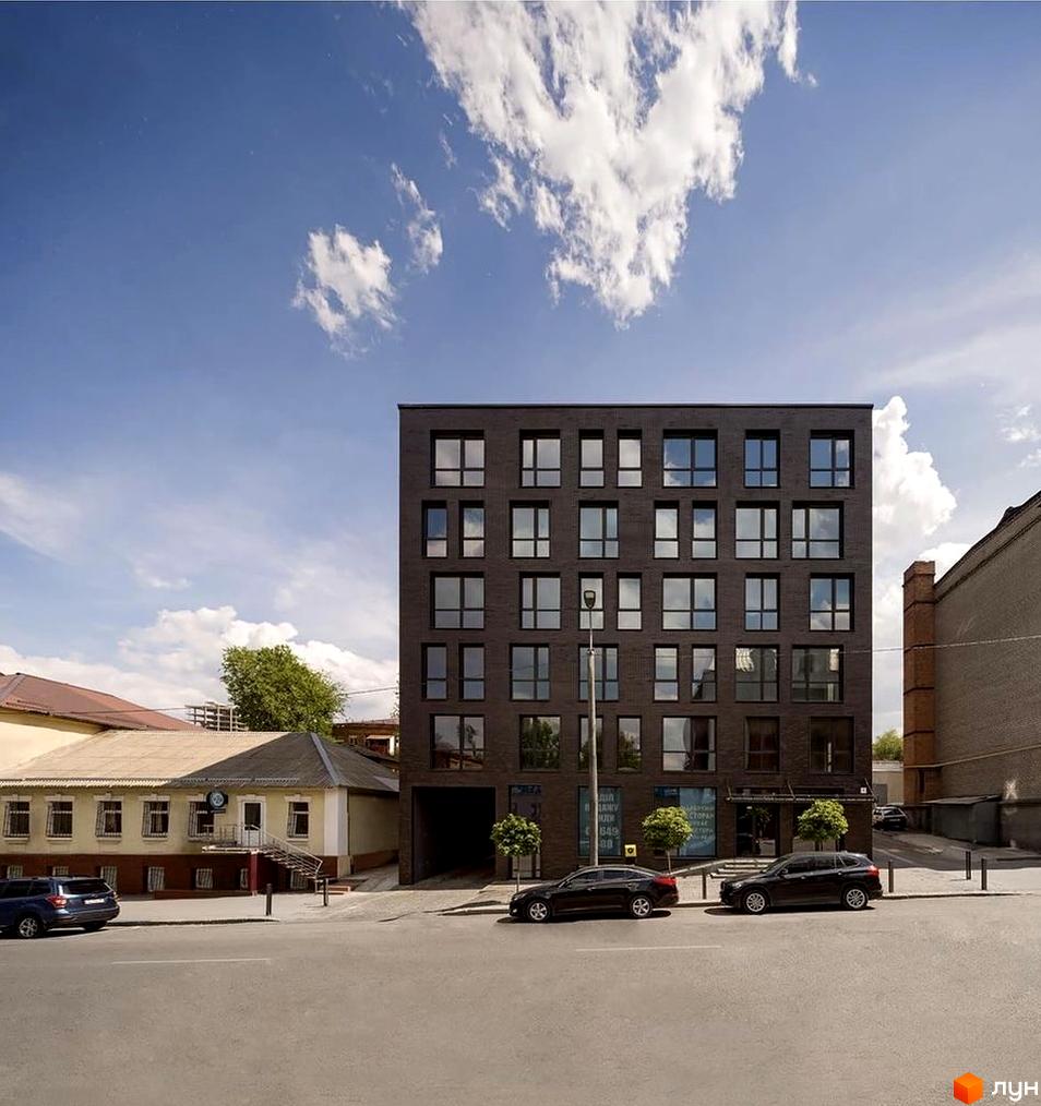 Фасад житлового комплексу ArtHof виконаний з темної цегли з великими вікнами. Перед будинком розташована дорога з припаркованими автомобілями та зелені насадження.