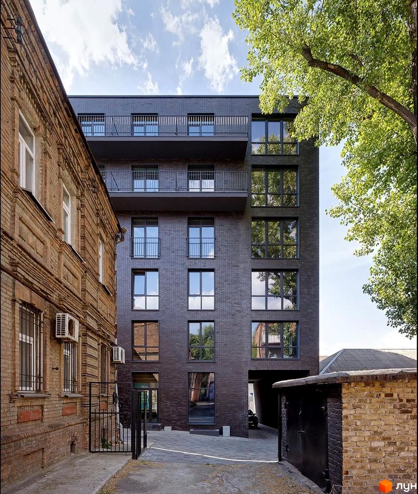 Темний цегляний багатоповерховий будинок Житлового комплексу ArtHof з великими вікнами та балконами. Поруч стара цегляна будівля та проїзд до паркінгу.