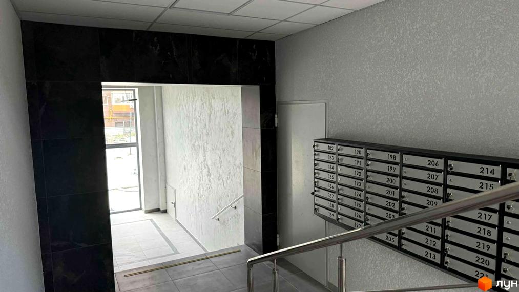 Під'їзд в ЖК Osnova з поштовими скриньками та сходовою кліткою. Зовнішній вигляд новобудови з сірими стінами та чорним оздобленням.